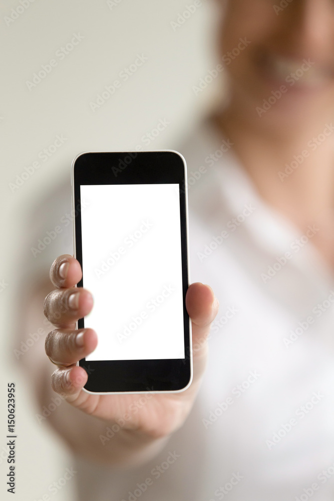 Close up image of cellphone in hand of blurred smiling woman on background. Female showing mock up blank touchscreen phone. Presenting new trendy model of electronic gadget. Mobile apps and service ad Close up image of cellphone in hand of blurred smiling woman on background. Female showing mock up blank touchscreen phone. Presenting new trendy model of electronic gadget. Mobile apps and service ad