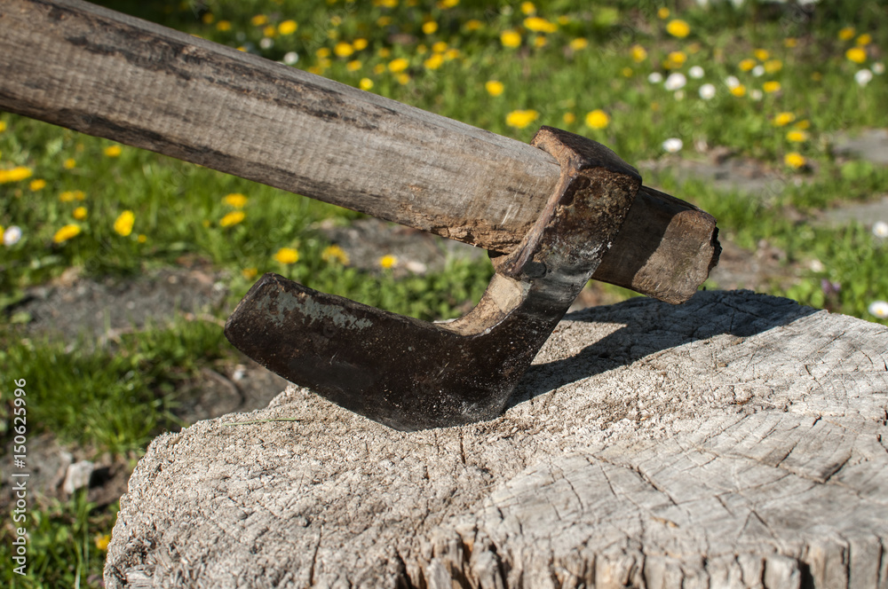 Old used weathered worn grunge metal ax stuck in wooden log closeup on rural background
