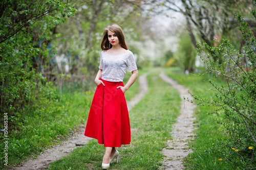 Portrait of beautiful girl with red lips at spring blossom garden, wear on red dress and white blouse.