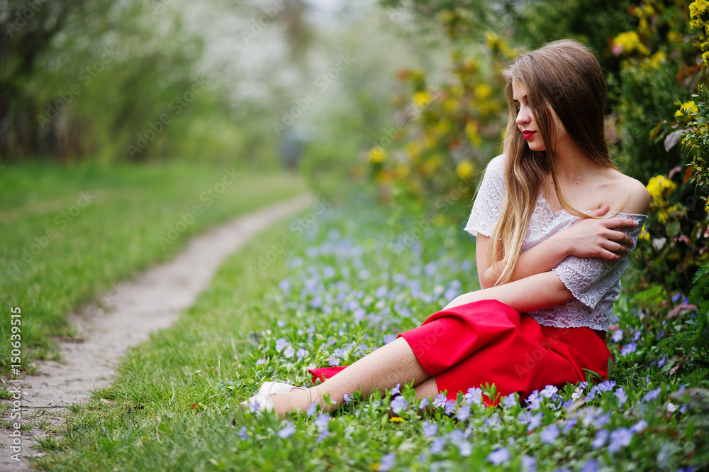 Portrait of sitiing beautiful girl with red lips at spring blossom garden on grass with flowers, wear on red dress and white blouse. Portrait of sitiing beautiful girl with red lips at spring blossom garden on grass with flowers, wear on red dress and white blouse.