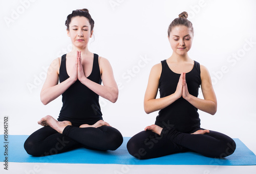 Young man and woman doing yoga and meditating in lotus position isolated on white background.