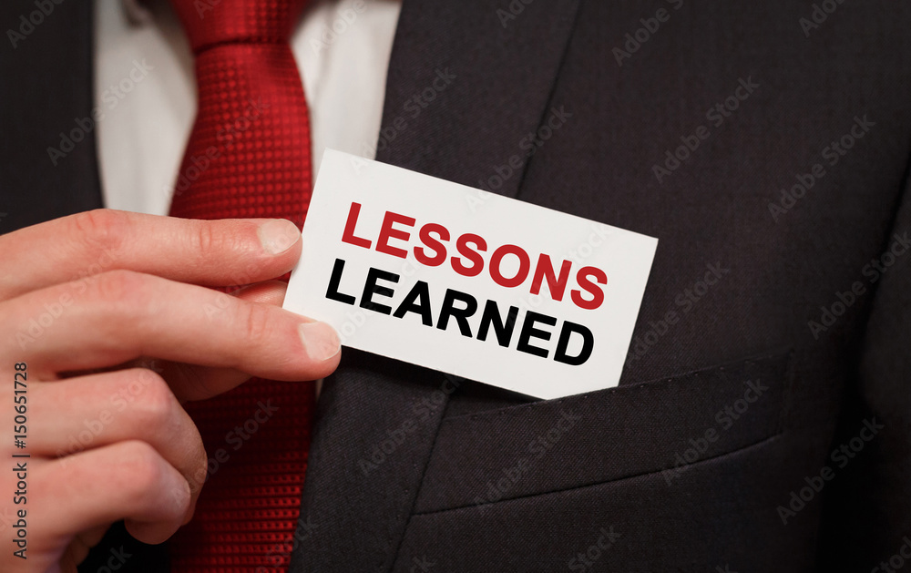 Businessman putting a card with text LESSONS LEARNED in the pocket Businessman putting a card with text LESSONS LEARNED in the pocket
