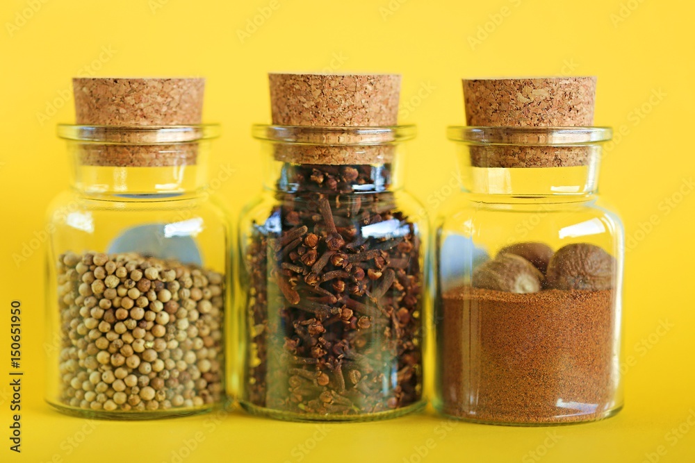 Nutmeg, white pepper and clove spice in a glass bottle on a bright yellow background Nutmeg, white pepper and clove spice in a glass bottle on a bright yellow background