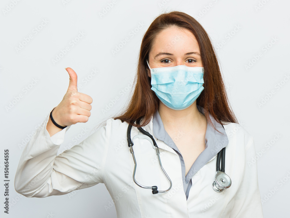 Beautiful female doctor with protecting medical mask showing thumbs up gesture on white background Beautiful female doctor with protecting medical mask showing thumbs up gesture on white background