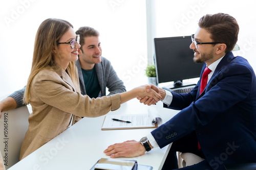 Fototapeta Young couple in bank office shaking hand to financial adviser.