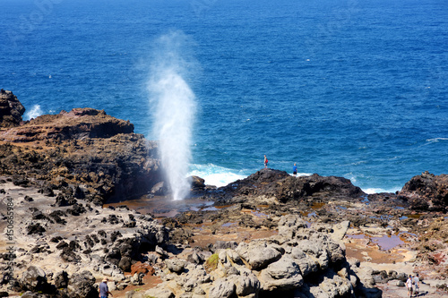 Tourists admiring the Nakalele blowhole on the Maui coastline. A jet of water and air is violently forced out through the hole in the rocks.