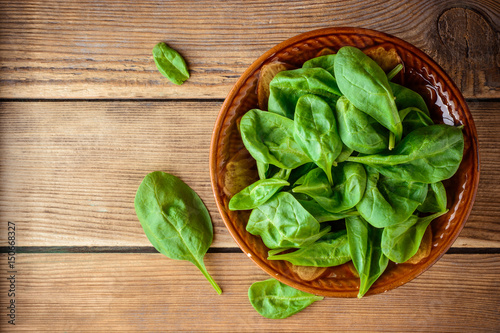 Fresh spinach leaves in bowl on rustic wooden table.