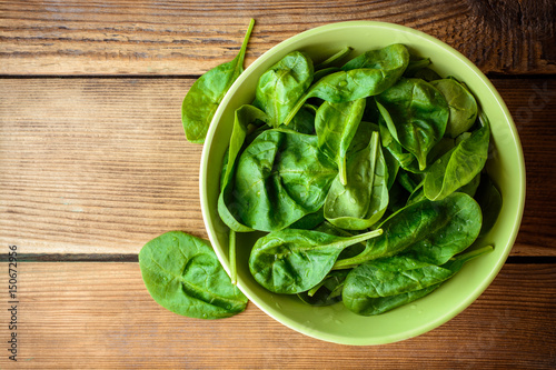 Washed fresh spinach leaves in bowl on rustic wooden table.