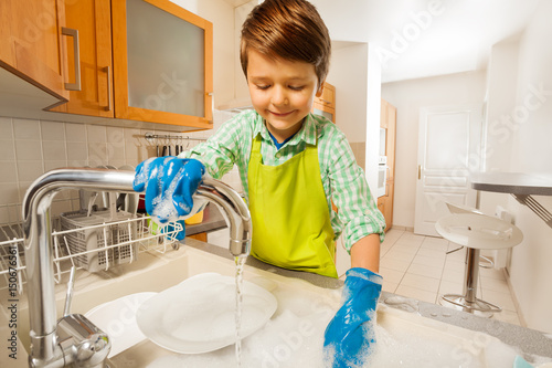 Canvastavla Happy kid boy rinsing dishes in the sink