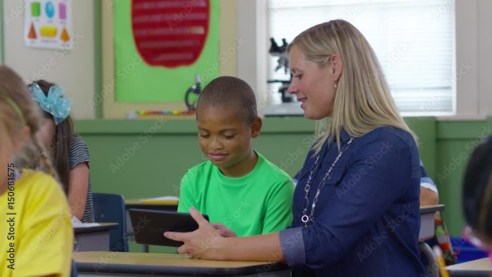 Teacher and student look at digital tablet in school classroom