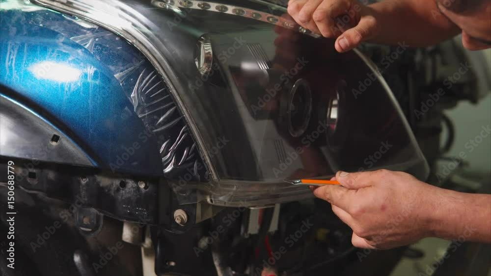 Close up shot of the hands of man who cut the vinyl film on the headlights of blue expensive car. This film protects the vehicle from the small chips and scratches. Close up shot of the hands of man who cut the vinyl film on the headlights of blue expensive car. This film protects the vehicle from the small chips and scratches.