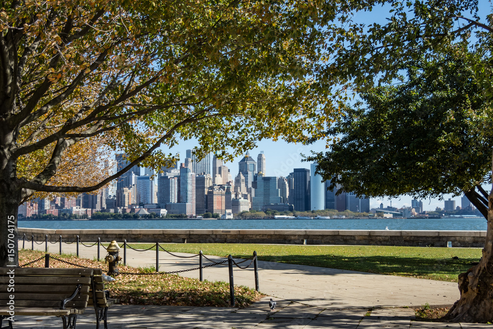 Obraz premium New York Manhattan Skyline seen from park on Ellis Island bench trees