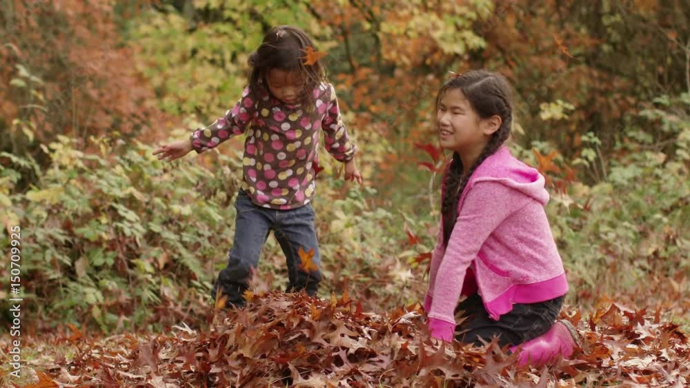 Two young girls in Fall throwing pile of leaves Two young girls in Fall throwing pile of leaves