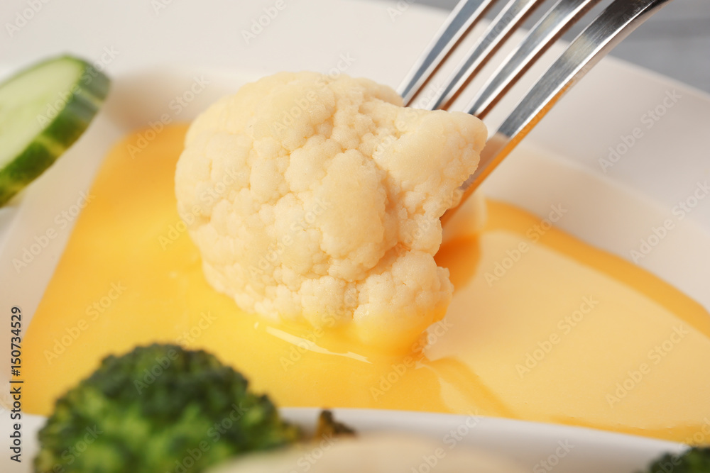 Fork with cauliflower dipped into cheese sauce, closeup Fork with cauliflower dipped into cheese sauce, closeup