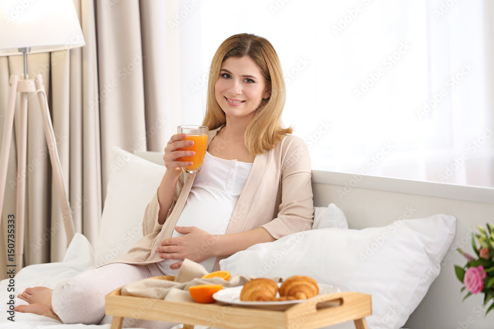 Young pregnant woman having breakfast while sitting on bed at home Young pregnant woman having breakfast while sitting on bed at home