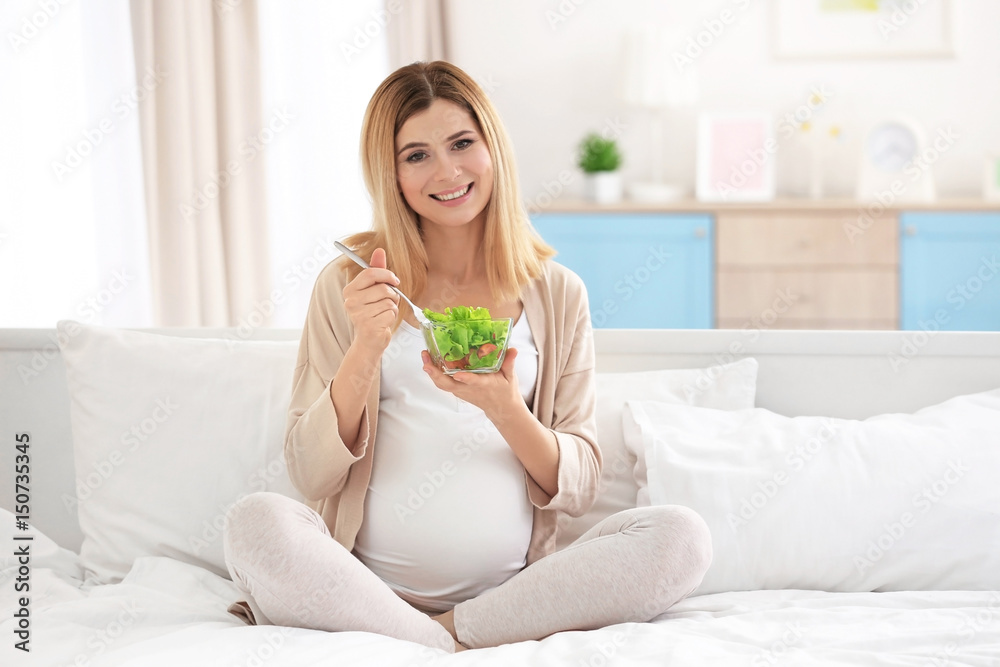 Young pregnant woman having breakfast while sitting on bed at home Young pregnant woman having breakfast while sitting on bed at home