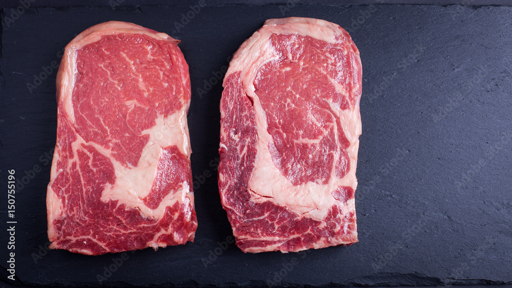 Two fresh raw marble meat, black Angus ribeye steak on a dark stone background.
