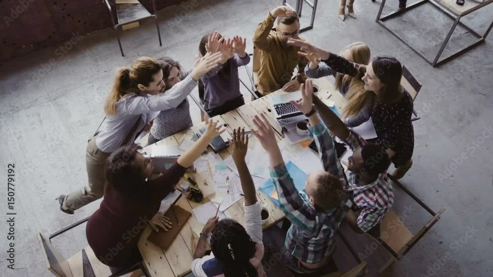 Top view of business team working at trendy loft office. Young mixed race group of people puts palm together on centre.