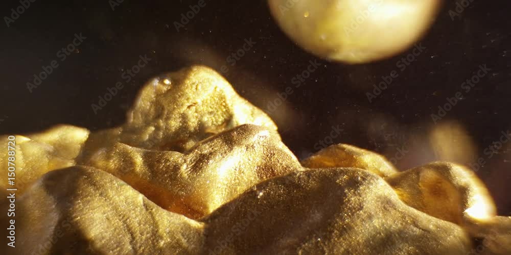 Abstract models mountains and planet made of golden plasticine, immersed in liquid. Closeup. 4K. Camera RED.
