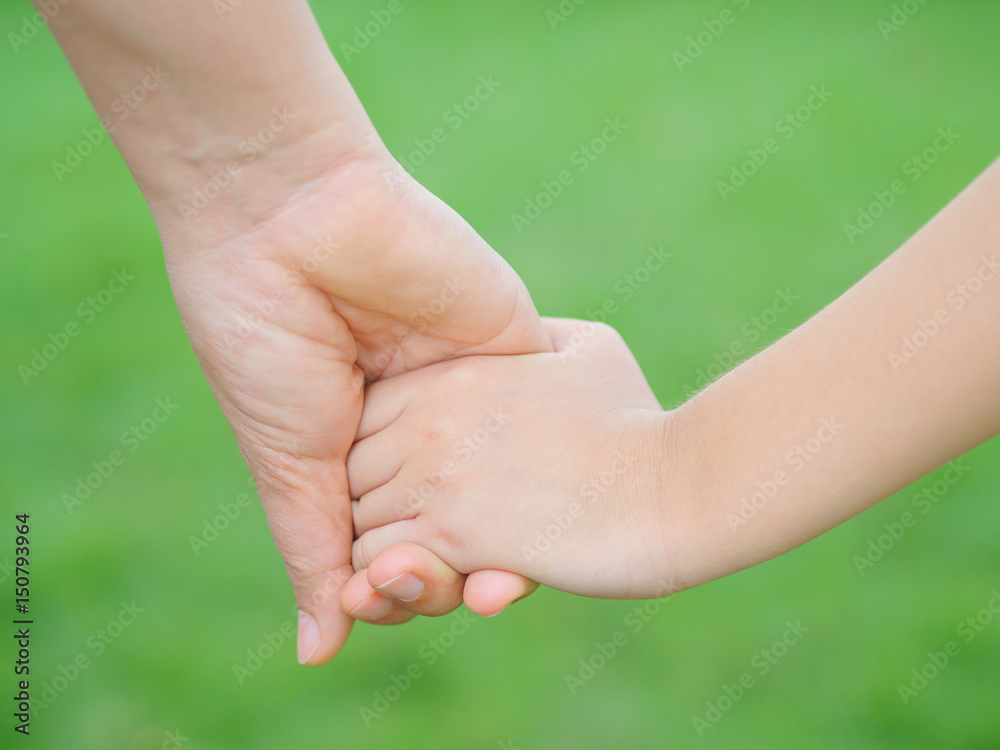Mother holding a hand of her kid in spring day outdoors with green field background Mother holding a hand of her kid in spring day outdoors with green field background