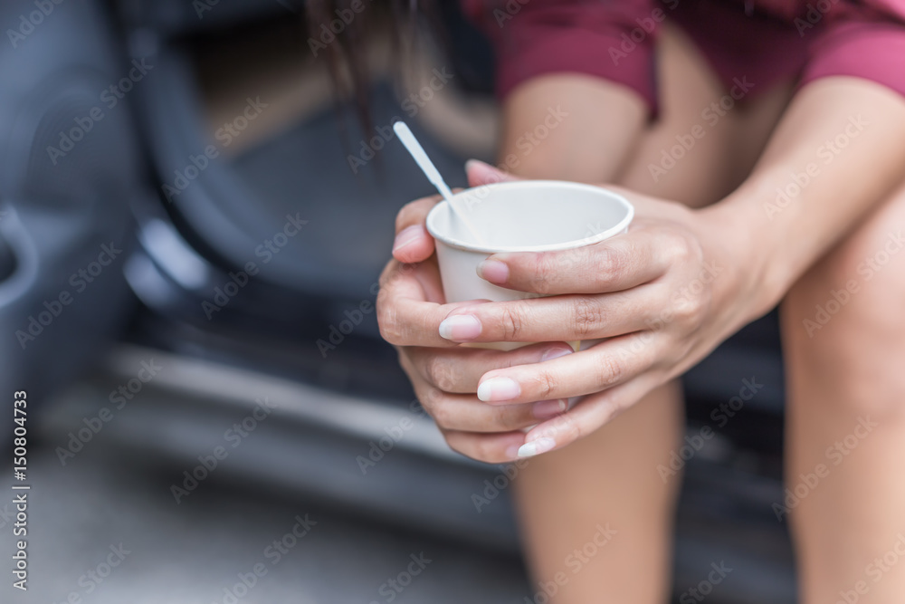 Woman sitting beside car and holding disposable cup of coffee Woman sitting beside car and holding disposable cup of coffee