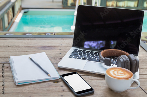 laptop coffee cup notepad smartphone and headphone at poolside