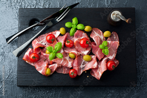 Dried meat, jamon with cherry tomatoes, basil and olives on a black background. Selective focus.Top view. Copy space.