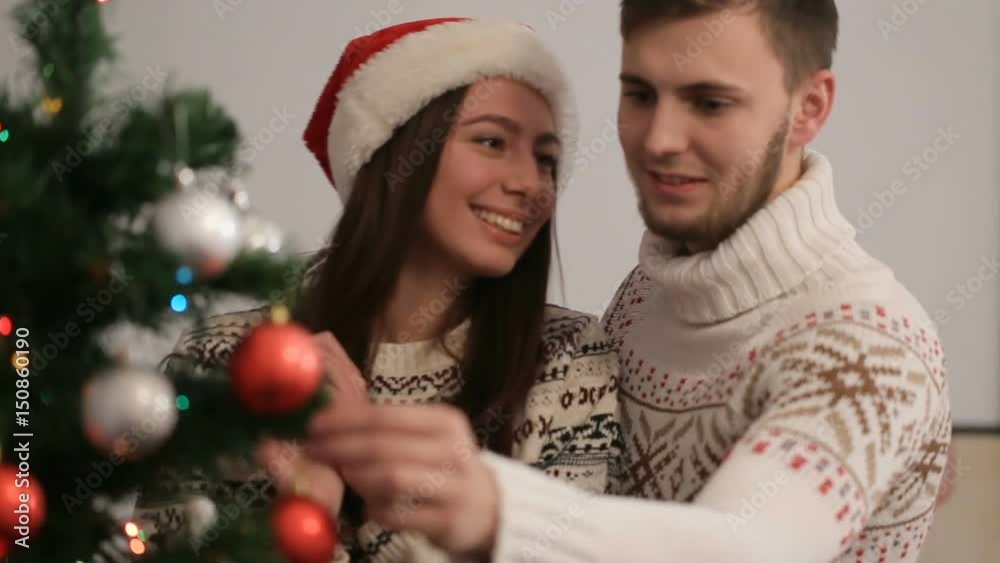 Happy young couple decorating christmas tree in cute sweaters. Couple in love preparing to the christmas eve. Happy young couple decorating christmas tree in cute sweaters. Couple in love preparing to the christmas eve.