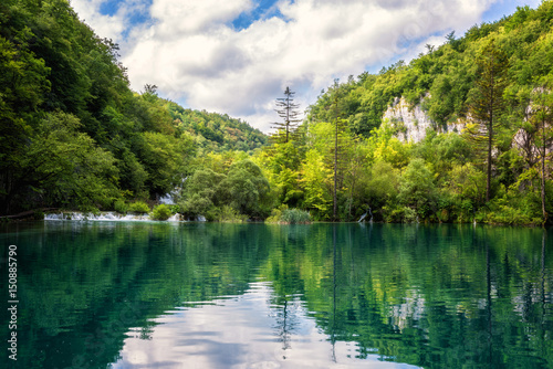 Fototapeta Naklejka Na Ścianę i Meble -  Plitvice Lakes National Park beautiful daytime landscape, green forest, waterfalls, blue cloudy sky and reflection in amazing green water of nature lake, image suitable for wallpaper or guide book