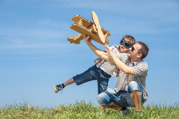 Father and son playing with cardboard toy airplane in the park at the day time.