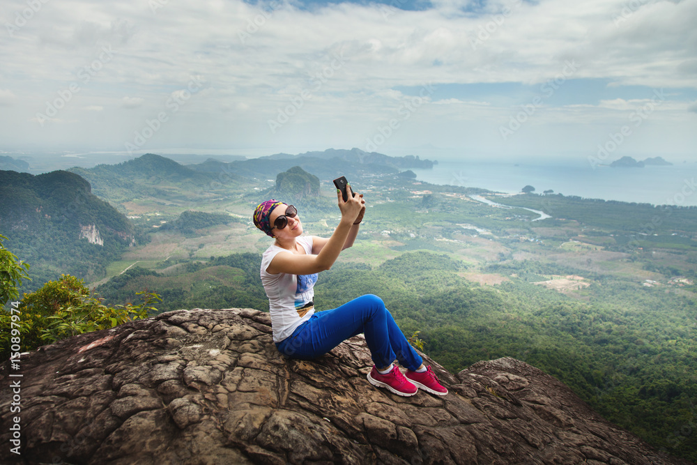 Women travel sit on a cliff on a rich forest mountain. Tab Kak Hang Nak Hill Nature Trail. Do selfie