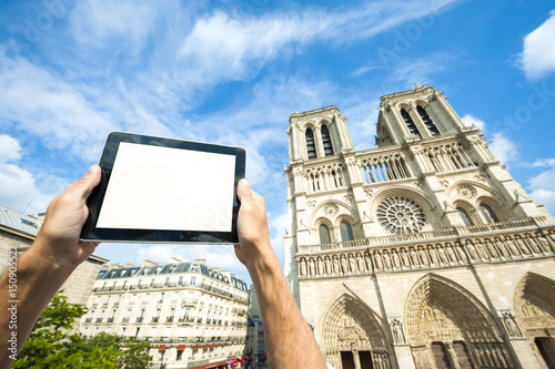 Hands holding blank screen tablet computer in front of the Cathedral of Notre Dame in Paris, France
