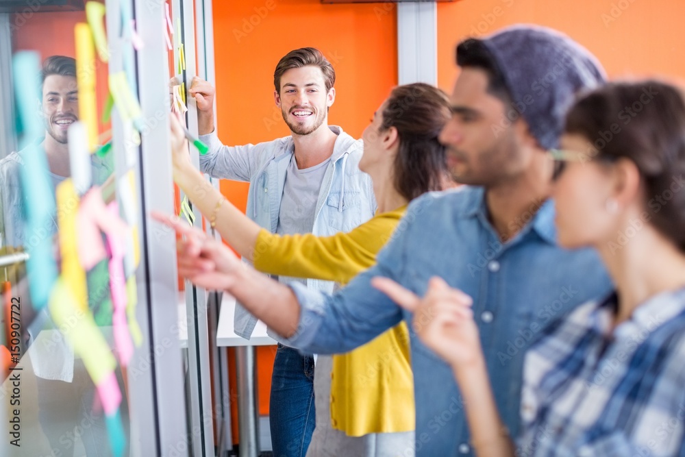 Obraz premium Smiling executives reading sticky notes on glass wall