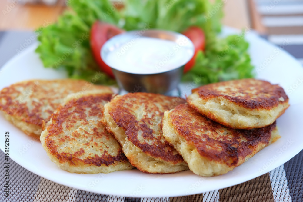 Potato pancakes served on plate with sour cream and salad leaves Potato pancakes served on plate with sour cream and salad leaves