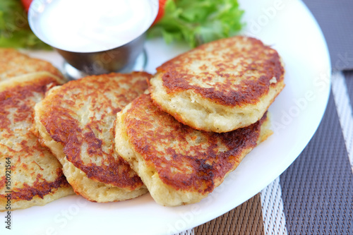 Potato pancakes served on plate with sour cream and salad leaves