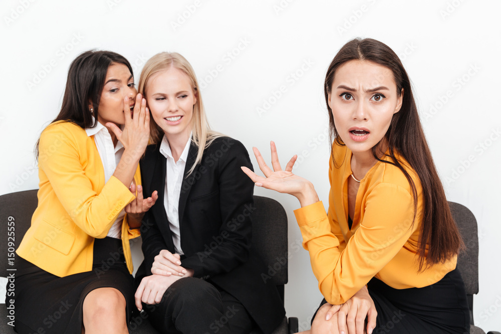 Confused woman sitting near happy colleagues women in office gossiping Confused woman sitting near happy colleagues women in office gossiping