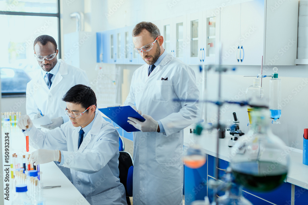 Professional scientists in white coats working together in chemical laboratory Professional scientists in white coats working together in chemical laboratory