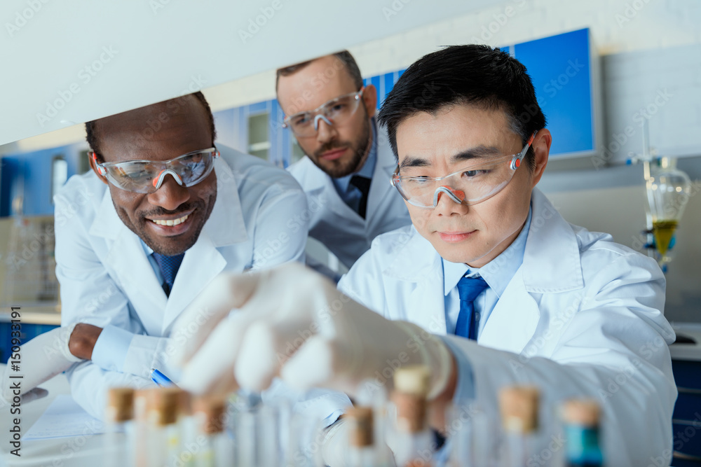 Multiethnic group of scientists in protective eyeglasses working together in chemical laboratory - obrazy, fototapety, plakaty 