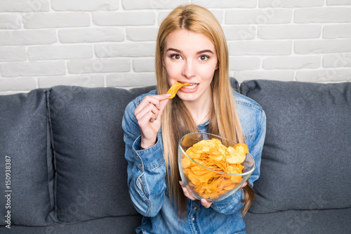Portrait of smiling girl eating chips at home on sofa photo