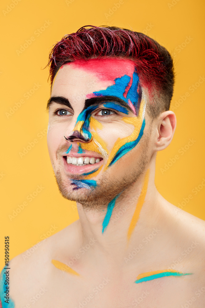 portrait of young man with colored face paint on yellow background. Professional Makeup Fashion. fantasy art makeup