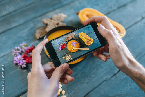 Close-up of man's hands taking picture of creamed pumpkin soup with smartphone photo