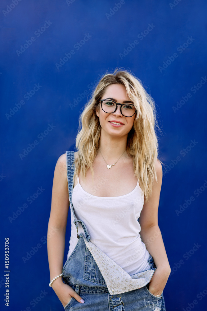 Young stylish blond girl in denim overalls made of denim and on a blue background Young stylish blond girl in denim overalls made of denim and on a blue background