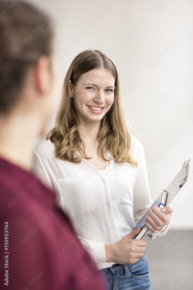 Portrait of smiling young businesswoman with notebook and clip board talking to colleague Portrait of smiling young businesswoman with notebook and clip board talking to colleague