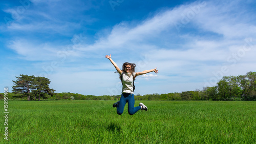 Happy Young Woman Jumping over blue sky. Beauty Girl Having Fun Outdoor. Freedom Concept. Nature