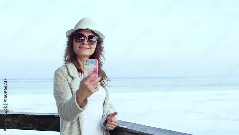 the young woman at the lighthouse makes a selfie with the hat. closeup the young woman at the lighthouse makes a selfie with the hat. closeup