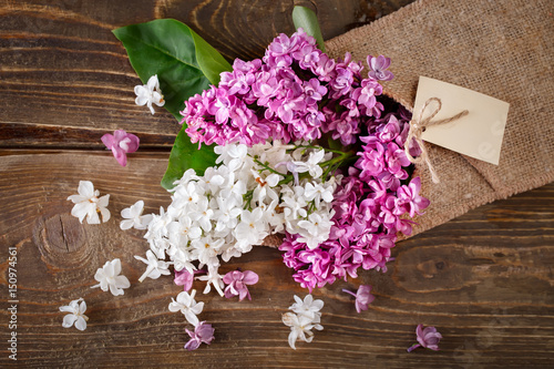 Branches of lilacs are in the basket of burlap on the background of wooden boards.
