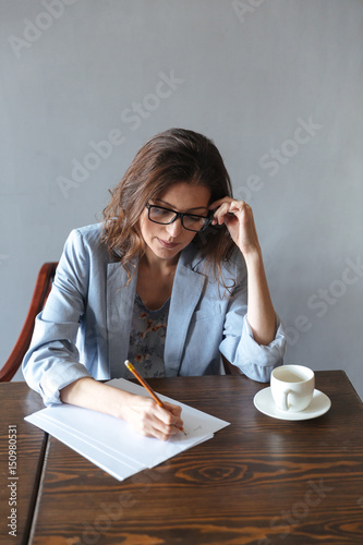 Concentrated woman writing notes indoors near cup of coffee