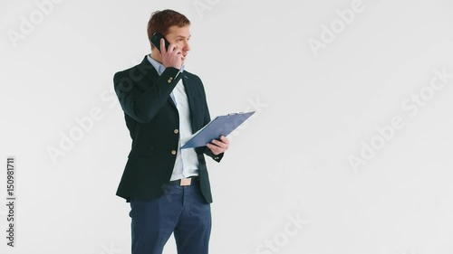 Young embarrassed sandsome man in suit discussing important serious business issues on the phone standing at whgite background photo