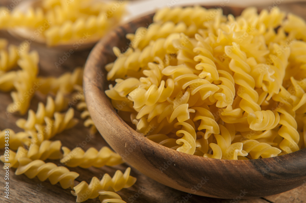 Pasta fusilli in a wooden bowl on wood background for healthy recipes. Pasta fusilli in a wooden bowl on wood background for healthy recipes.
