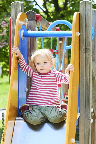 Happy little toddler blond girl having fun sliding on playground